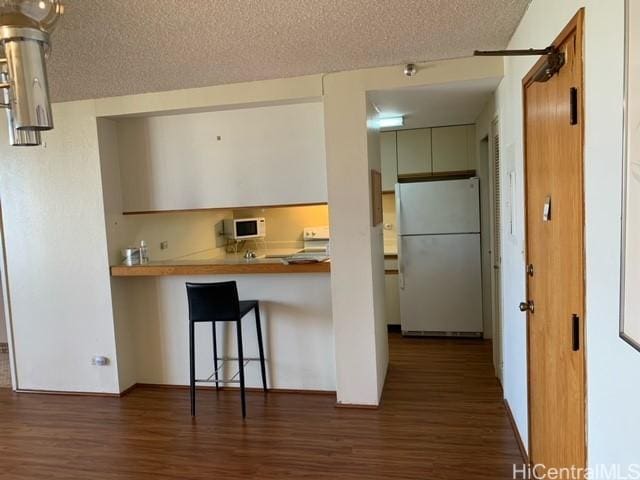 5333 Likini St Unit 2103, Honolulu, HI 96818 - kitchen featuring freestanding refrigerator, wood finished floors, a breakfast bar, a textured ceiling, and a peninsula