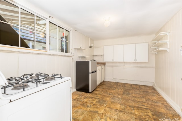 kitchen featuring white range with gas stovetop, white cabinetry, wood walls, and stainless steel refrigerator