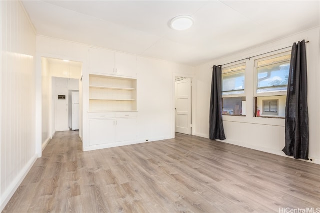 spare room with light wood-type flooring and built in shelves