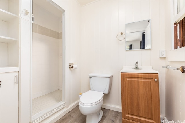 bathroom featuring a tile shower, wood walls, toilet, vanity, and hardwood / wood-style flooring