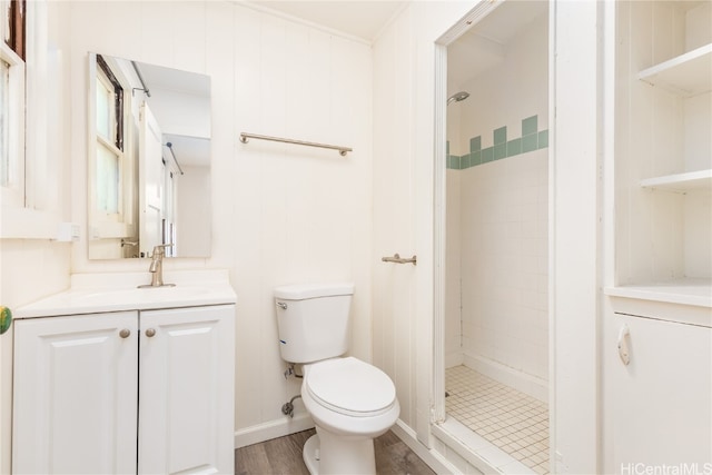 bathroom with wood-type flooring, toilet, tiled shower, vanity, and wooden walls