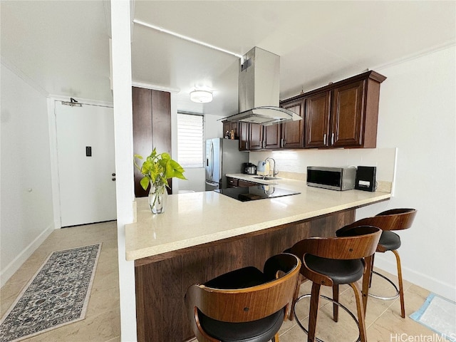 kitchen featuring dark brown cabinetry, island exhaust hood, stainless steel appliances, a kitchen bar, and a sink