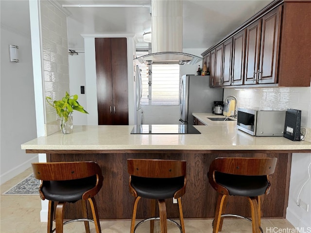 kitchen featuring island range hood, a sink, light countertops, appliances with stainless steel finishes, and backsplash