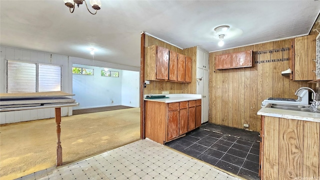 kitchen featuring dark colored carpet, light countertops, a sink, brown cabinets, and wooden walls
