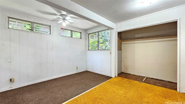 unfurnished bedroom with dark carpet, wood walls, a closet, and ceiling fan