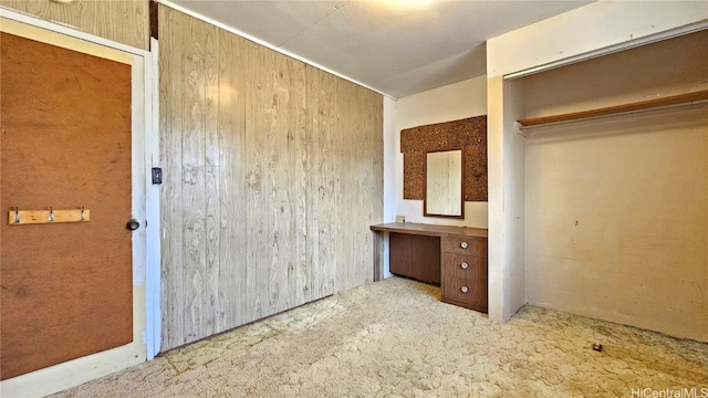 unfurnished bedroom with light carpet, a closet, and wooden walls