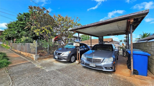 view of parking with driveway, a carport, and fence