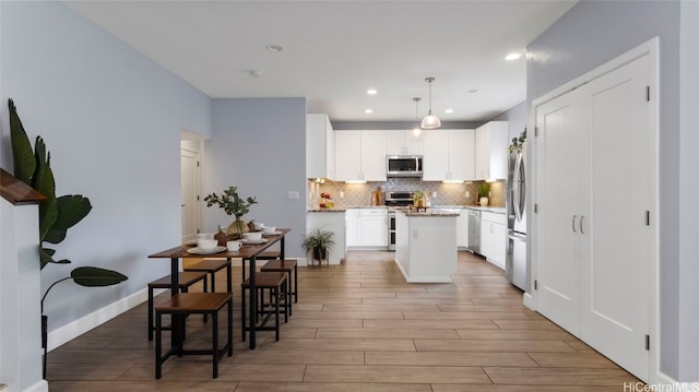 kitchen featuring a kitchen island, light hardwood / wood-style flooring, hanging light fixtures, white cabinetry, and appliances with stainless steel finishes