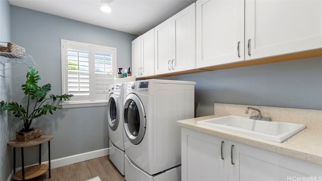 clothes washing area with washing machine and dryer, sink, light wood-type flooring, and cabinets