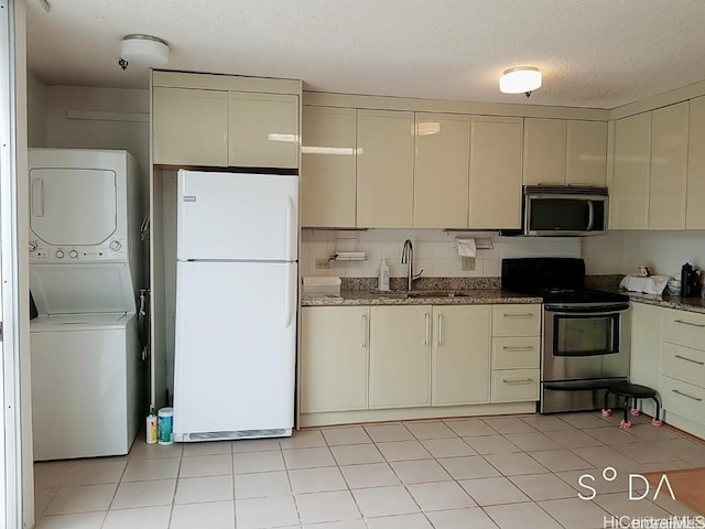 kitchen featuring stacked washer and clothes dryer, cream cabinetry, stainless steel appliances, sink, and a textured ceiling