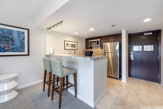 kitchen with kitchen peninsula, decorative backsplash, a breakfast bar area, appliances with stainless steel finishes, and dark brown cabinetry