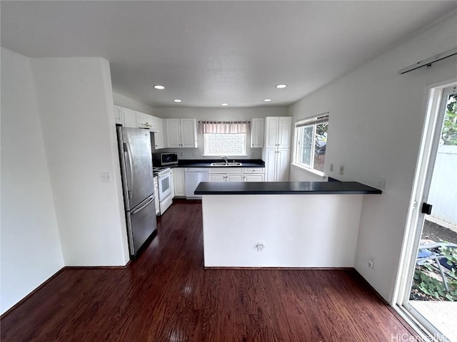 kitchen with sink, stainless steel appliances, dark hardwood / wood-style floors, kitchen peninsula, and white cabinets