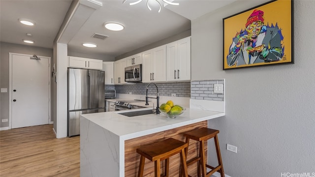 kitchen with kitchen peninsula, white cabinetry, stainless steel appliances, decorative backsplash, and a breakfast bar area