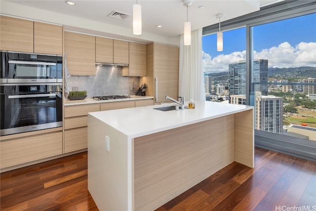 kitchen with a kitchen island with sink, sink, dark wood-type flooring, and pendant lighting