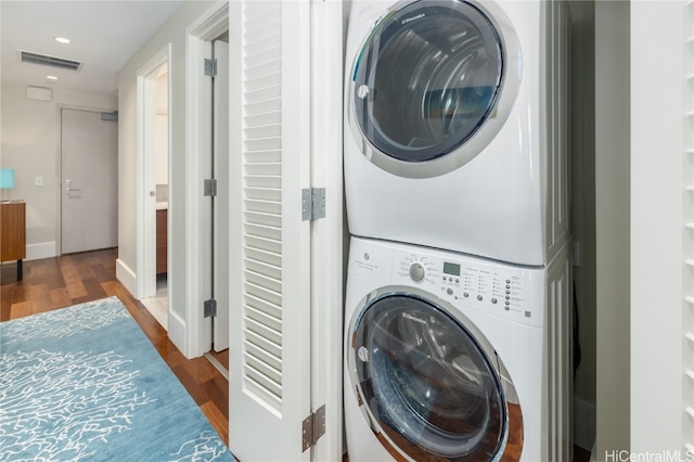 clothes washing area featuring stacked washer and dryer and dark hardwood / wood-style flooring