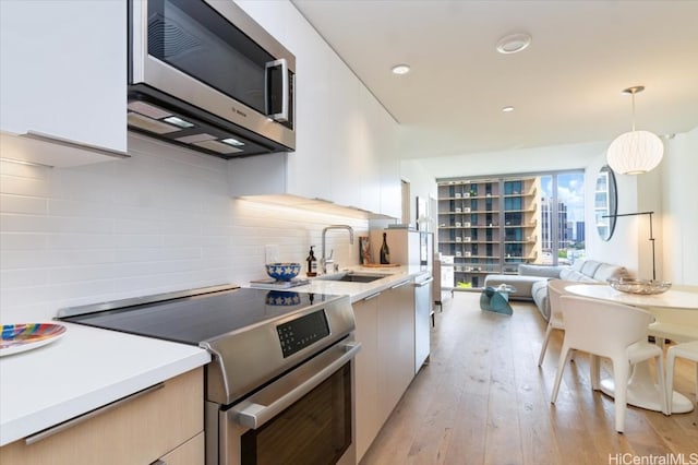 kitchen with hanging light fixtures, white cabinetry, sink, light hardwood / wood-style floors, and stainless steel appliances