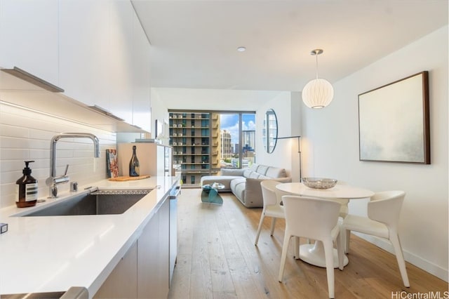 kitchen featuring backsplash, white cabinetry, pendant lighting, light hardwood / wood-style floors, and sink