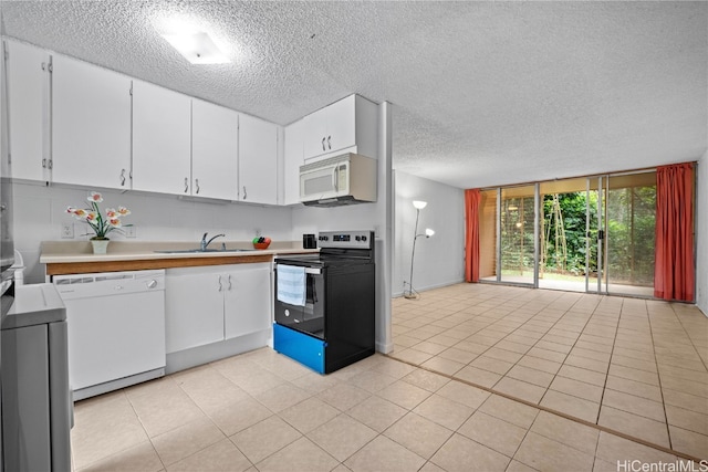 kitchen with white appliances, sink, light tile patterned floors, a textured ceiling, and white cabinetry