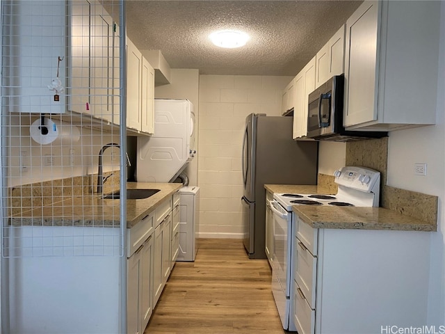 kitchen with white cabinets, white range with electric cooktop, stacked washer / dryer, and sink