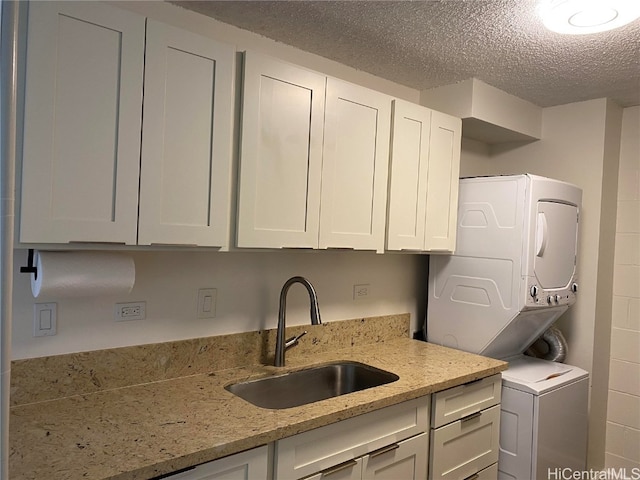 kitchen featuring white cabinets, sink, light stone countertops, and stacked washer and dryer