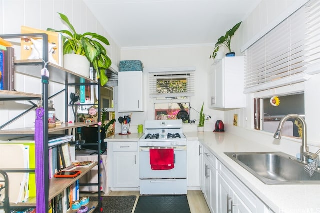 kitchen with white gas stove, sink, white cabinetry, ornamental molding, and light hardwood / wood-style flooring