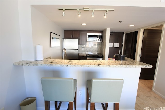 kitchen with decorative backsplash, a breakfast bar area, light stone countertops, light hardwood / wood-style floors, and stainless steel appliances