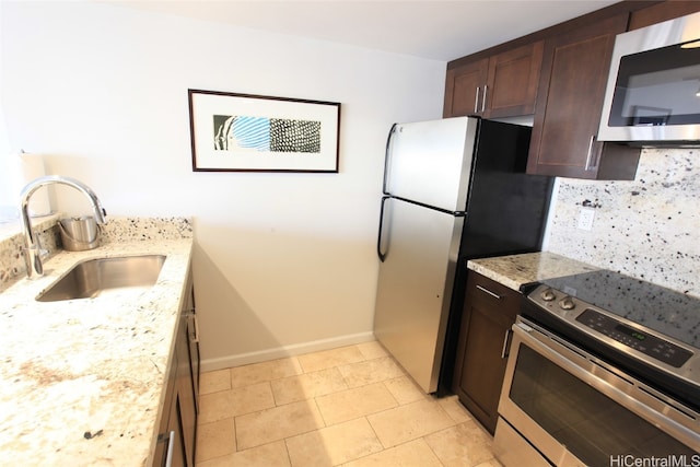 kitchen with sink, stainless steel appliances, light stone counters, decorative backsplash, and light tile patterned floors