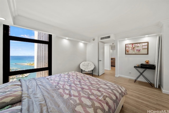 bedroom with ornamental molding, a water view, and light hardwood / wood-style floors