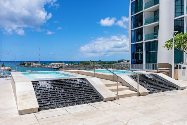 view of swimming pool featuring a water view, a patio area, and a jacuzzi