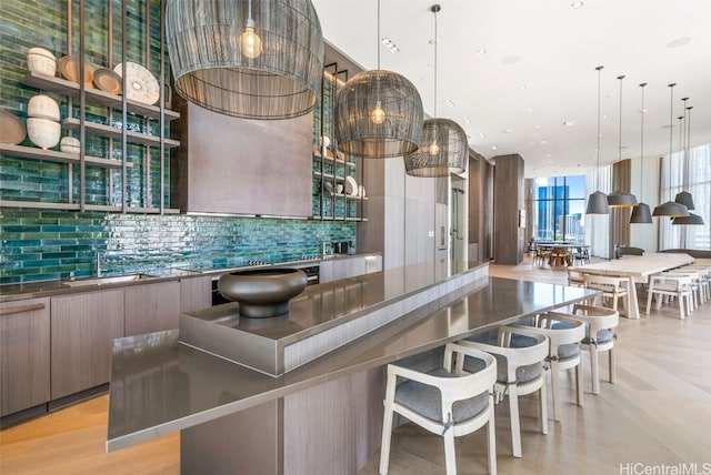 kitchen with tasteful backsplash, sink, a spacious island, hanging light fixtures, and light hardwood / wood-style flooring