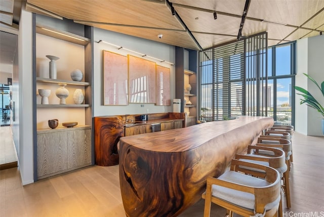 dining space with a high ceiling, a wall of windows, light wood-type flooring, and wood ceiling