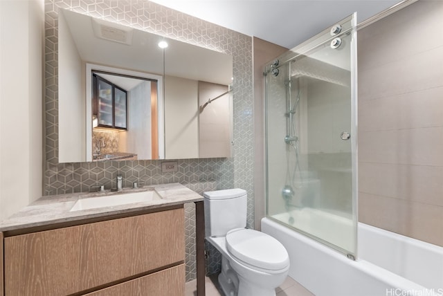 full bathroom with decorative backsplash, toilet, vanity, tile walls, and shower / bath combination with glass door