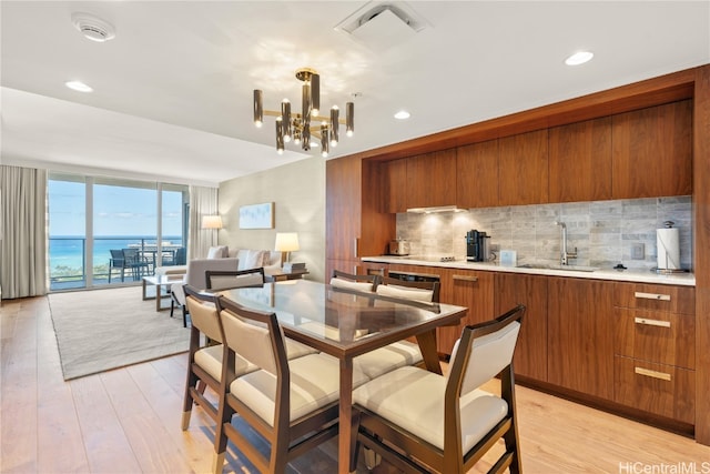 dining space with light hardwood / wood-style flooring, a chandelier, sink, and a water view