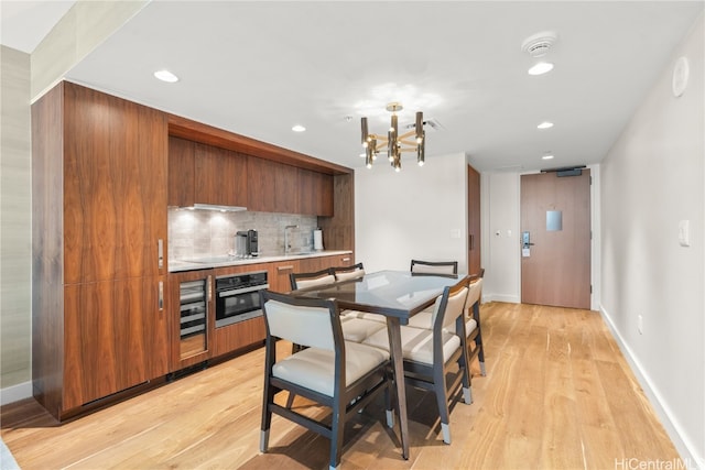 kitchen with backsplash, stainless steel oven, a notable chandelier, light hardwood / wood-style flooring, and exhaust hood