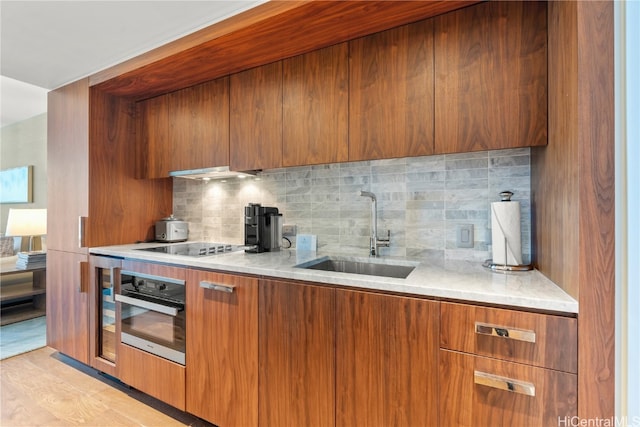 kitchen with tasteful backsplash, oven, sink, stovetop, and light hardwood / wood-style flooring