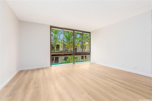 unfurnished room featuring light wood finished floors, baseboards, and floor to ceiling windows
