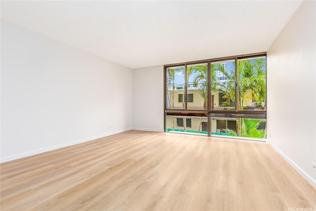 empty room featuring light wood finished floors, expansive windows, and baseboards