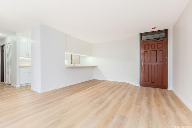 empty room featuring light wood-type flooring, baseboards, and a sink