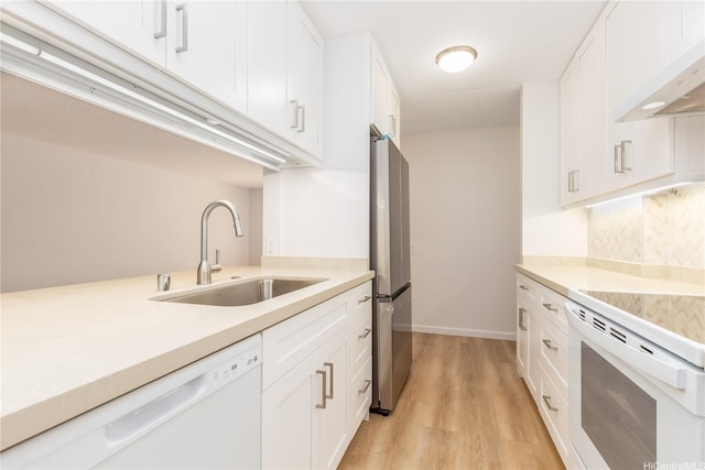 kitchen with light wood finished floors, under cabinet range hood, light countertops, white appliances, and a sink