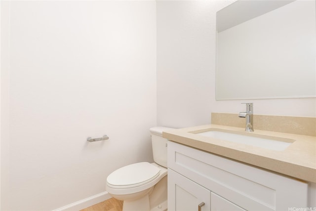 half bath with baseboards, toilet, vanity, and wood finished floors