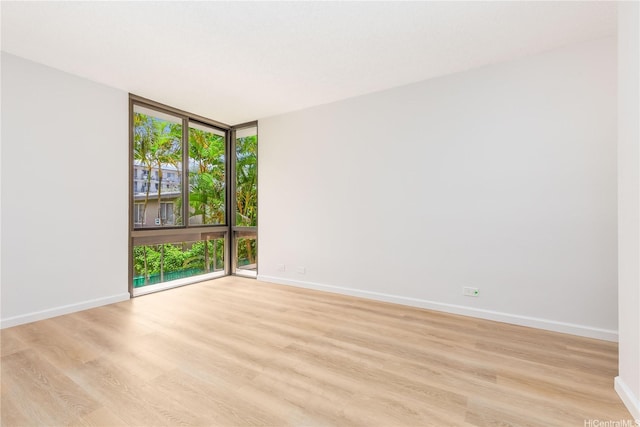 spare room featuring baseboards, light wood-style flooring, and floor to ceiling windows