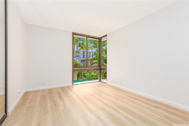 spare room with expansive windows, light wood-style floors, and baseboards