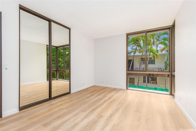 empty room featuring baseboards, a wall of windows, wood finished floors, and a wealth of natural light