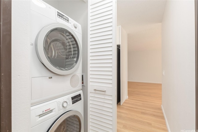 washroom with baseboards, stacked washer / drying machine, laundry area, and light wood-style flooring