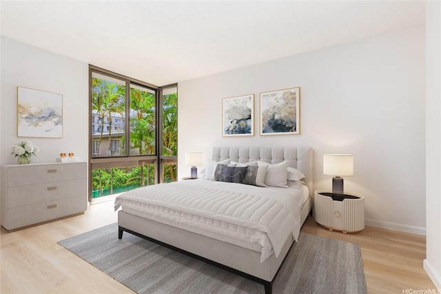 bedroom featuring light wood-type flooring, baseboards, floor to ceiling windows, and multiple windows