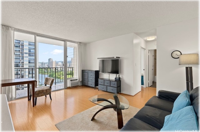 living room with light hardwood / wood-style floors, a textured ceiling, an AC wall unit, and floor to ceiling windows