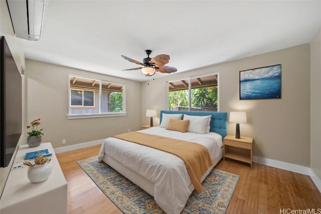 bedroom with ceiling fan, light hardwood / wood-style floors, and a wall mounted air conditioner