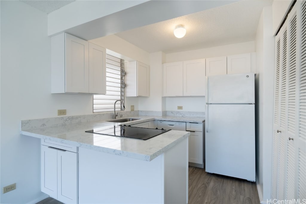 kitchen with sink, kitchen peninsula, white cabinets, dark wood-type flooring, and white refrigerator