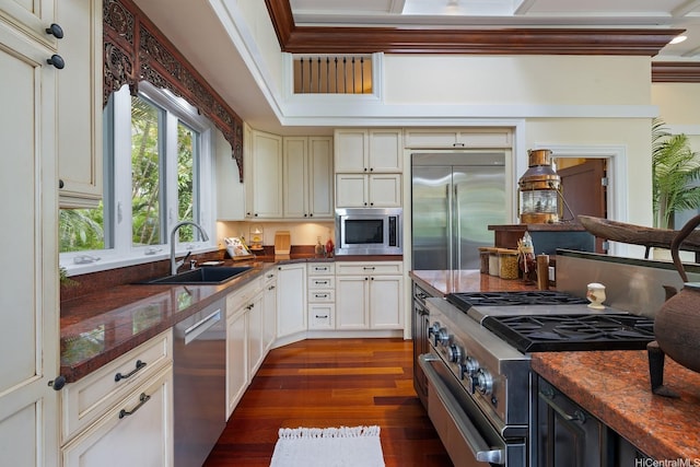 kitchen featuring a sink, dark wood finished floors, dark countertops, built in appliances, and crown molding