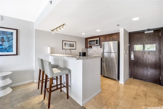 kitchen featuring kitchen peninsula, tasteful backsplash, a kitchen bar, dark brown cabinetry, and stainless steel appliances